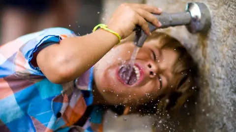 Un niño se refresca bebiendo agua de la fuente