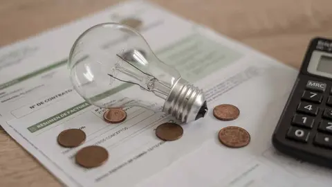 Factura de electricidad, LUZ, con bombilla varias monedas y calculadora en el escritorio. Propiedad renatahamuda Descarga Freepik premium 26.11.24